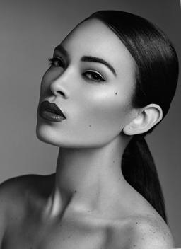 Black and white beauty portrait of brunette Asian looking woman with full, dark lips and low ponytail