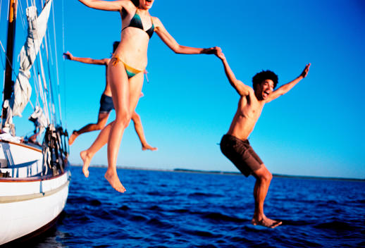 exterior motion shot of young smiling Caucasian woman in bikini and young smiling African American man in swim trunks jumping into ocean