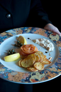 Hands holding a chef plated dinner of Atlantic salmon dill gravlax, cr?me fraiche and house made potato chips.