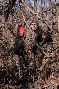 Two men hide in the woods while on a hunt.