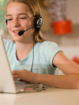 Smiling girl wearing earphones and microphone sitting at desk typing on a laptop computer