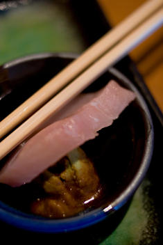 Chopsticks Along Side A Slice Of Yellowtail Sashimi Dipped In Soy Sauce And Wasabi