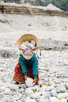 An elderly Nepalese woman picks up a rock to carry out in her basket in the sand mines in Pokhara, Nepal.