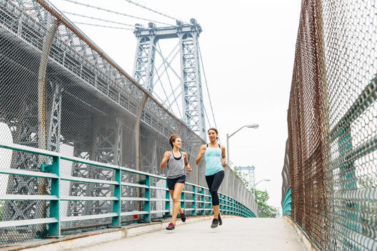Two women running over a bridge with the Manhattan bridge in the background.