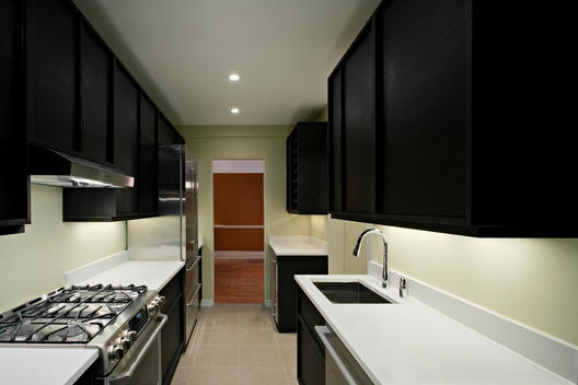 Empty, Dark Paneled Kitchen With All New Fixtures, Illuminated Hallway In Background