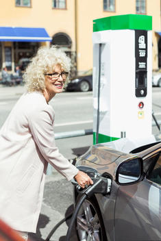 Smiling senior woman filling car with petrol at gas station