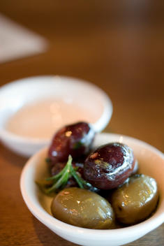 A Small Bowl Of Olives Garnished With Rosemary On A Table Top, Served As An Appetizer At An Italian Restaurant.