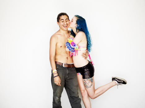A portrait of a purple haired girl giving a guy a kiss at an electronic music festival in new York