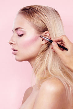 Close-up up of blonde model in clean bare skin and light pink eyeshadow and pink blush