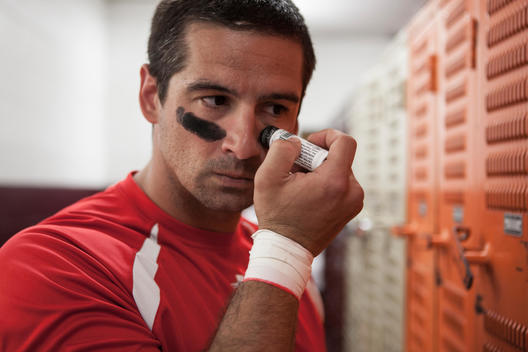 A football player puts on eye black before a game in the locker room.