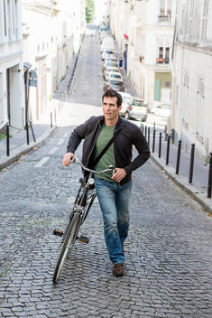 Mid adult man pushing bicycle up cobbled city street