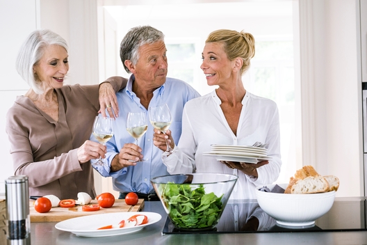 Happy senior couple and mature woman raising a glass of wine to each other in kitchen