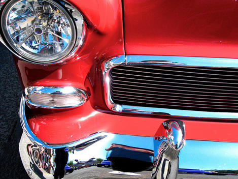 The front of a red car with shiny chrome bumper and grill