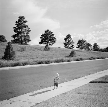 A curious, adventurous lone baby boy innocently runs to the edge of the sidewalk of his family's suburban home trying to cross the unsafe street to Bow Mar Heights Park on a bright sunny summer day. Denver, Utah