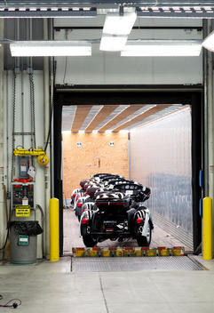 Inside the Harley Davidson factory several 3 wheeled motorcycles get loaded into the back of a tractor trailer