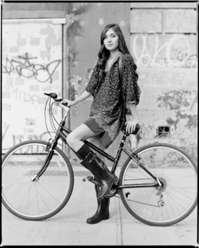 A Young European Woman Rides Her Bicycle In Front Of A Run-Down Dilapidated Building With Graffiti Near Union Square During A Fashion Shoot For Clothing Brand Callalilai. New York City.