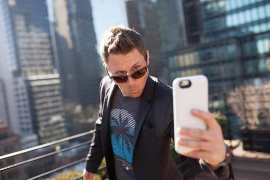 Portrait of business and tech entrepreneur Casey Kerr taking a funny selfie with his cell phone on the rooftop popular hotel Pod 51 with view of midtown east Manhattan. NYC