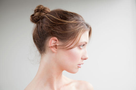 Close up beauty shot of a girl with hair tied up in front of a white wall in natural light.