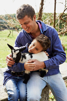 a father and son holding a baby goat in their arms