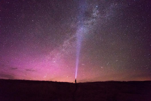 shining a flashlight at the milky way in the night sky lit pink by the norther lights