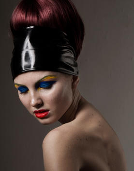 Studio beauty tight crop portrait of a female model with her hair pulled into a bun with bright colored dramatic makeup in a dramatic sculptural pose looking down over her shoulder