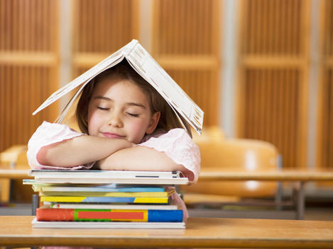 Girl (4-7) sitting desk, leaning on stack of books, eyes closed