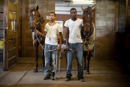 Environmental portrait of two African American teenagers posing with horses at a stable