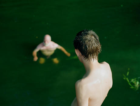 A Young Man Watches An Old Man Swimming In A River.