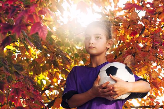 Girls by tree covered in autum leaves holding football looking away