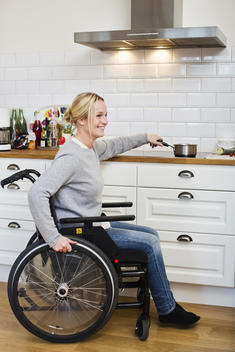Happy disabled woman in wheelchair preparing tea at kitchen