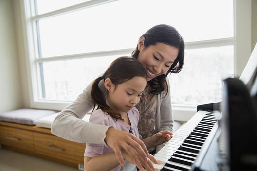 Mother teaching daughter to play piano