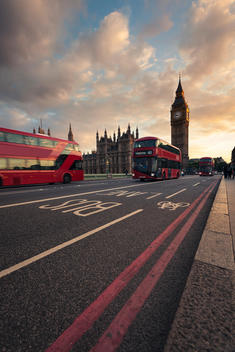 UK, London, red buses passing Westminster Bridge with Big Ben tower in the background at sunset
