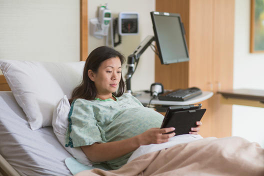 Pregnant Chinese woman in hospital room using digital tablet