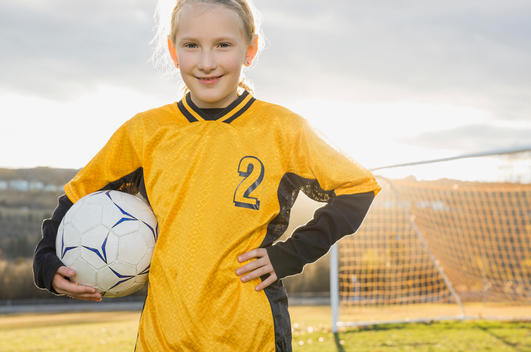 Confident soccer player with ball standing on field