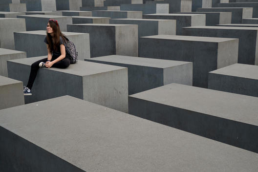 The Holocaust Memorial designed by the architect Peter Eisenman. A girl sitting on one of the grey concrete steal blocks.