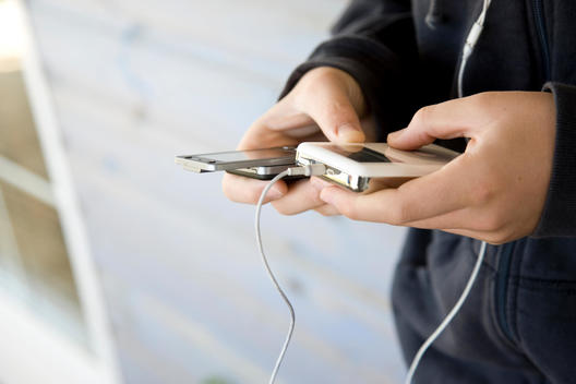 Close up of a boy\'s hands holding a cell phone and a portable audio player