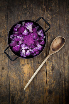 Cooking pot of purple cauliflower florets and wooden spoon on wood