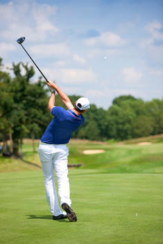 Golfer hitting ball with a driver, shot from behind