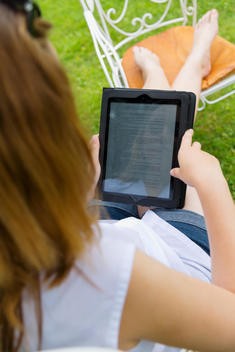 Young woman sitting in a garden chair using digital tablet, partial view