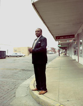 An African American Man Dressed In His Sunday Best Standing On A Sidewalk Clasping His Hands.
