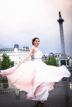 Portrait of young woman dancing in evening gown at dusk, Trafalgar Square, London, UK