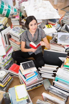 Smiling young woman sitting in the middle of piles of books