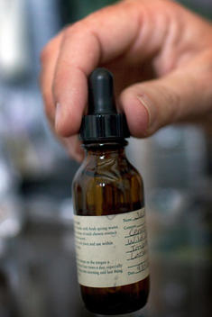 Hand Holding A Small Brown Bottle Containing A Homeopathic Remedy.