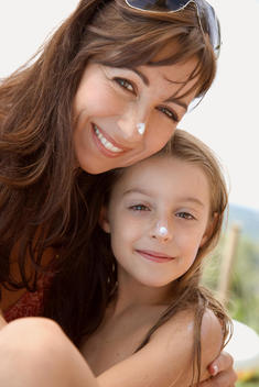 Portrait of mother and daughter embracing with sunscreen lotion on nose
