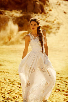 All in white a female model walks along the desert in the late sun.