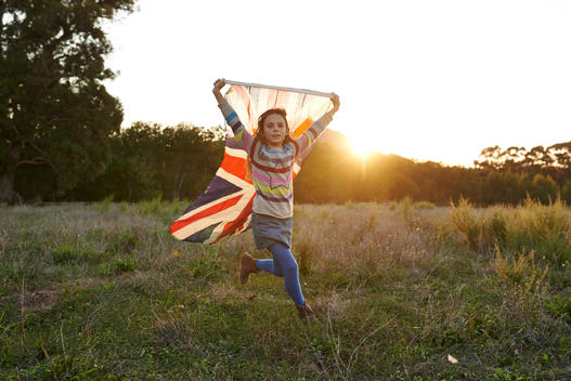 girl running with english flag on a grass field on sunset