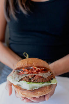 Woman Holding A Vegetarian Hamburger With Grilled Onions, Lettuce And Cheese