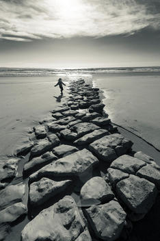 A young child five years old runs across a limestone pavement on a sandy beach