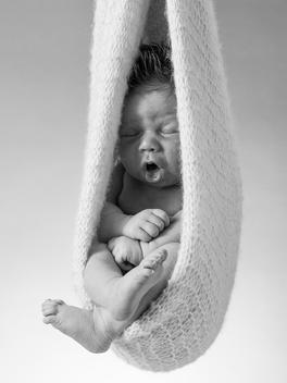 New born baby yawning whilst hanging in knitted blanket.