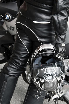 A leather motorcycle rider with his back turned holding a helmet in his hand next to his motorcycle